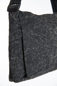 Close-up of the black ebb and flow messenger bag with a subtle gray swirl pattern,