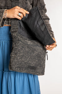 Close view of black cotton messenger bag showing textured fabric and exterior zipper pocket