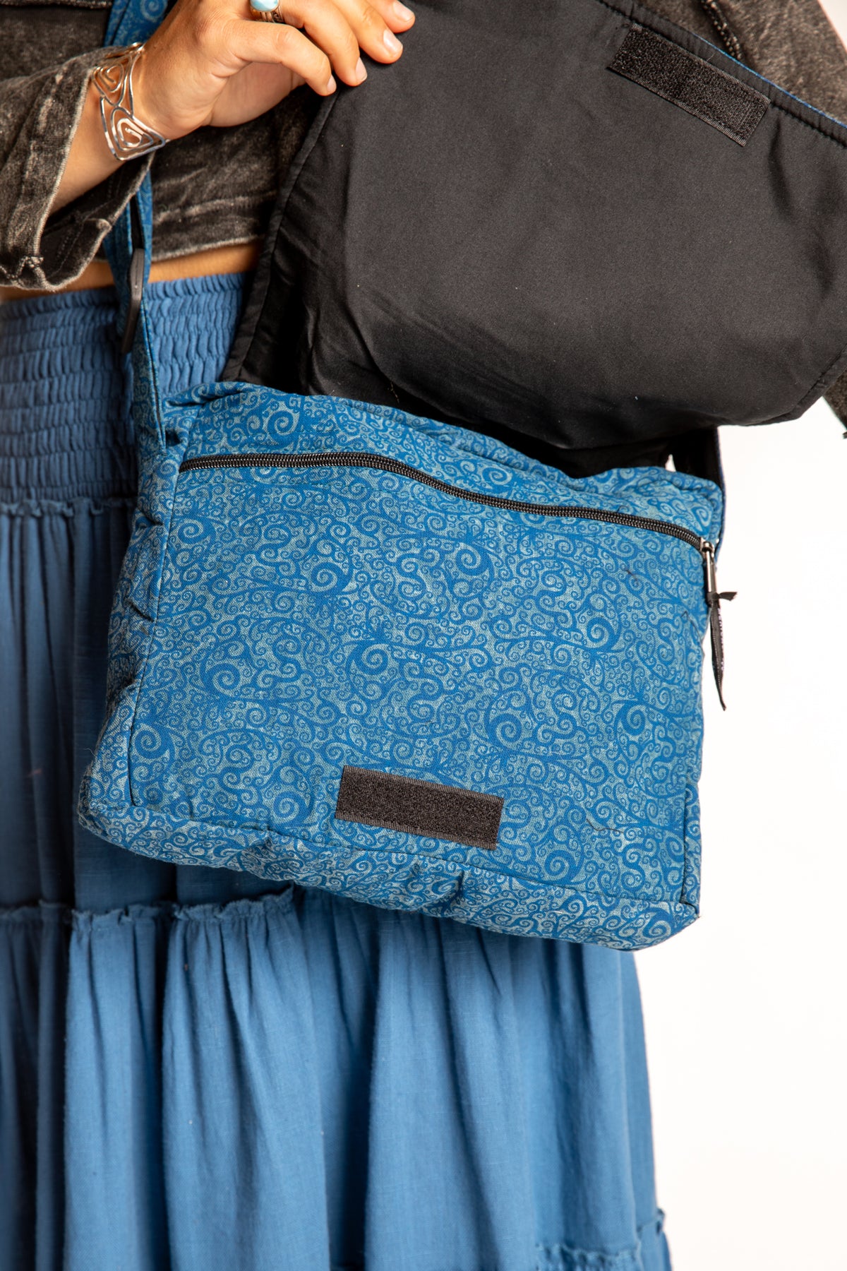 A blue ebb and flow messenger bag with a black zipper and a small brown patch
