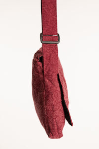A red ebb and flow messenger bag  with a subtle swirl pattern and adjustable strap