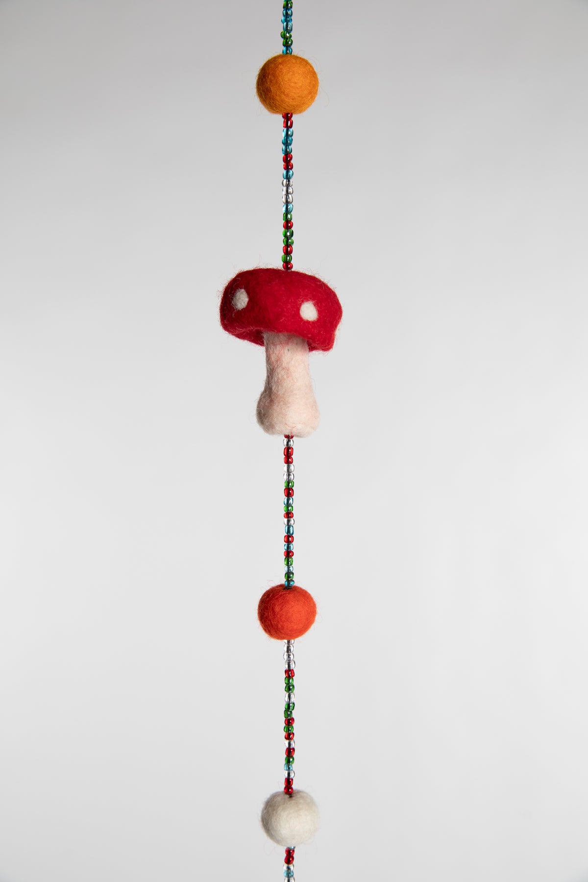 A closeup of the beaded garland with felt balls and red and white felted mushrooms 