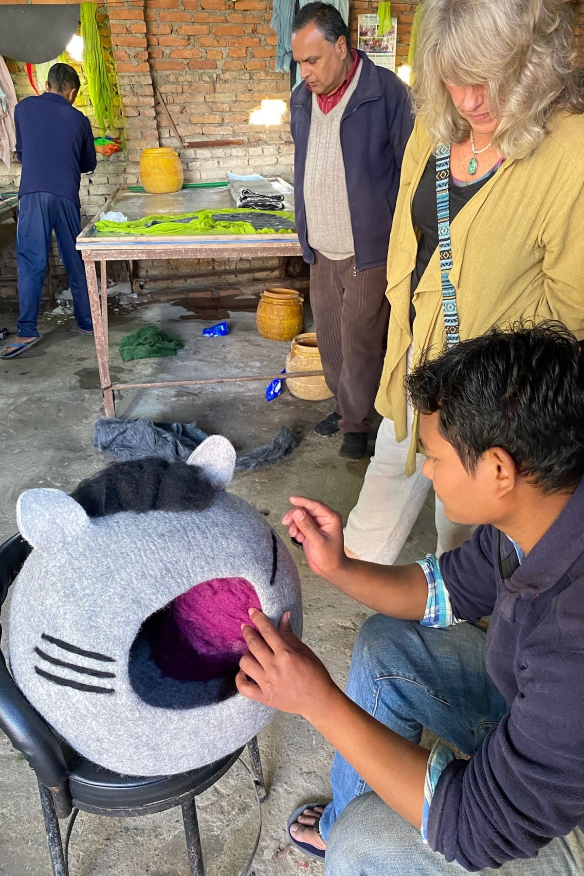 A man working on a gray felted cat cave with onlookers