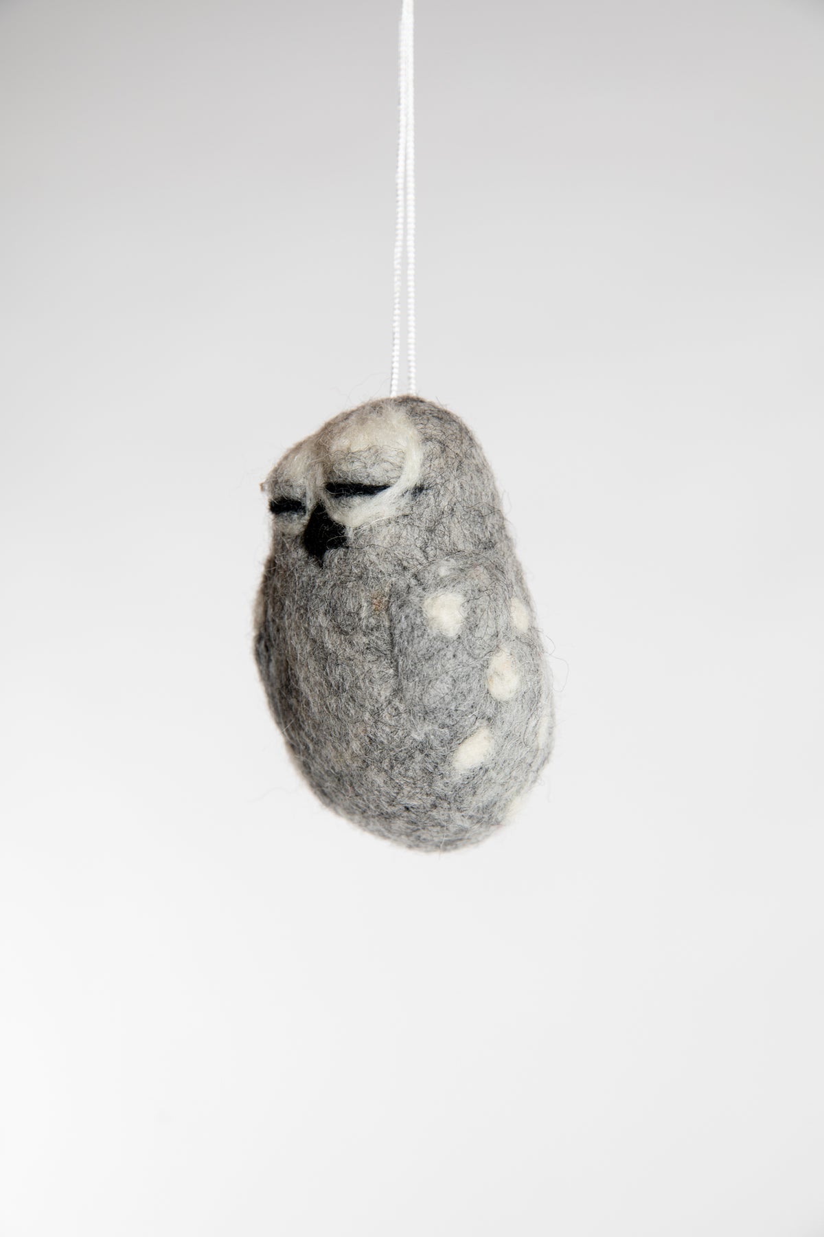 Sideview of a small and grey felted owl with closed eyes