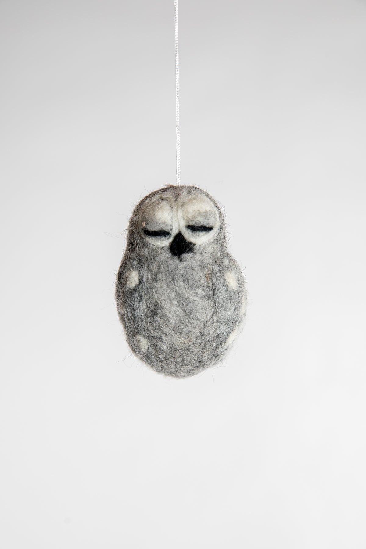 A small and grey felted owl ornament with closed eyes
