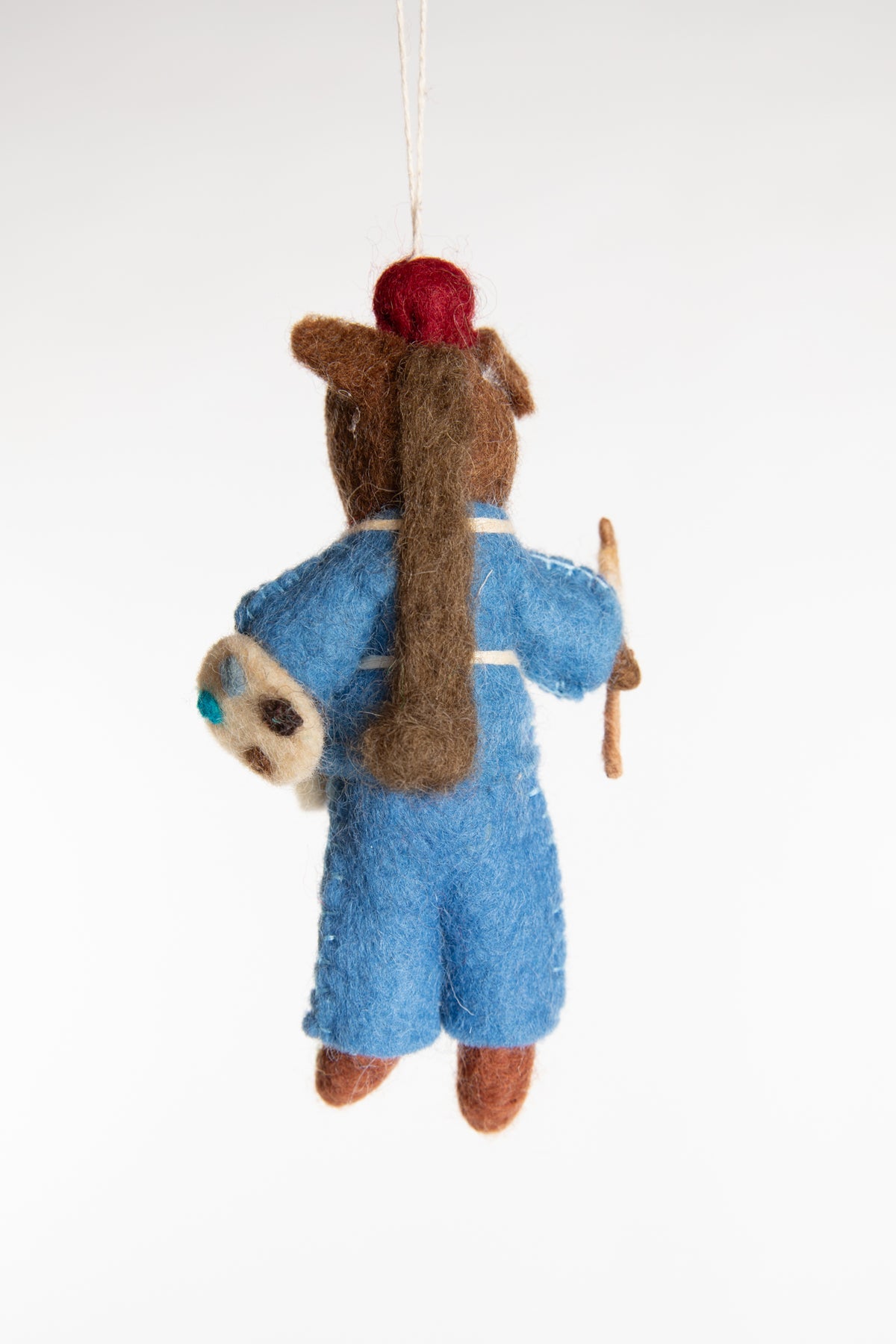 The back of a felted horse ornament with blue overalls, holding a palette and paintbrush