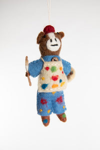 A felted horse ornament with blue overalls, holding a palette and wearing a painter's apron covered in paint spots