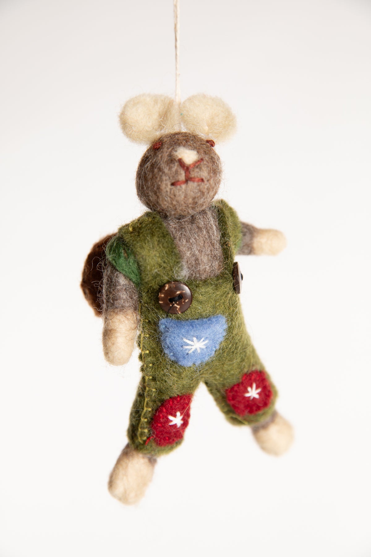 The front of a felted wool mouse ornament with a brown backpack and wearing green overalls with red and blue patches