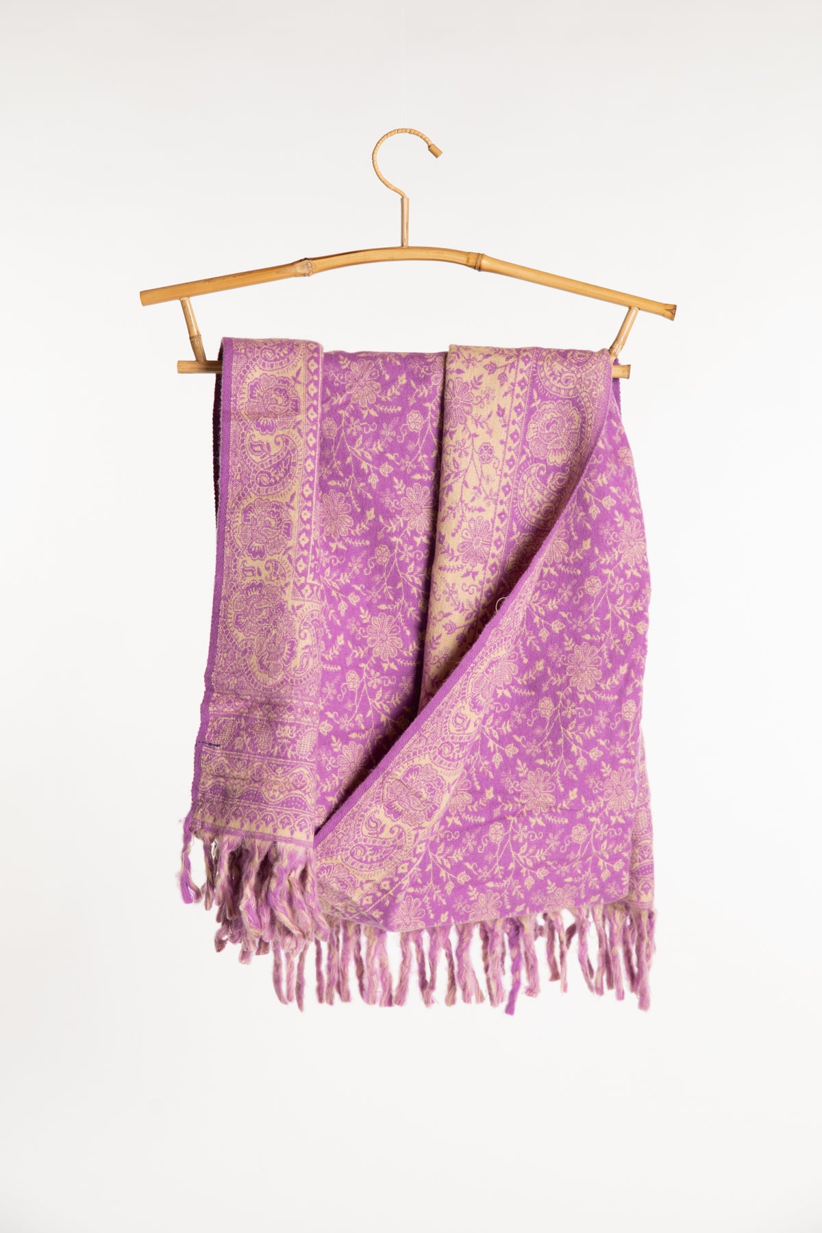 The lavender paisley soft brushed shawl with fringe, draped over a bamboo hanger against a plain white background.