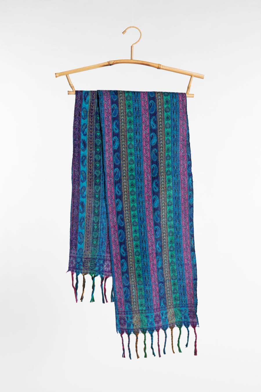 The blue striped soft brushed scarf in shades of blue, purple, and green with tassels, hanging from a light wood hanger against a plain white background.