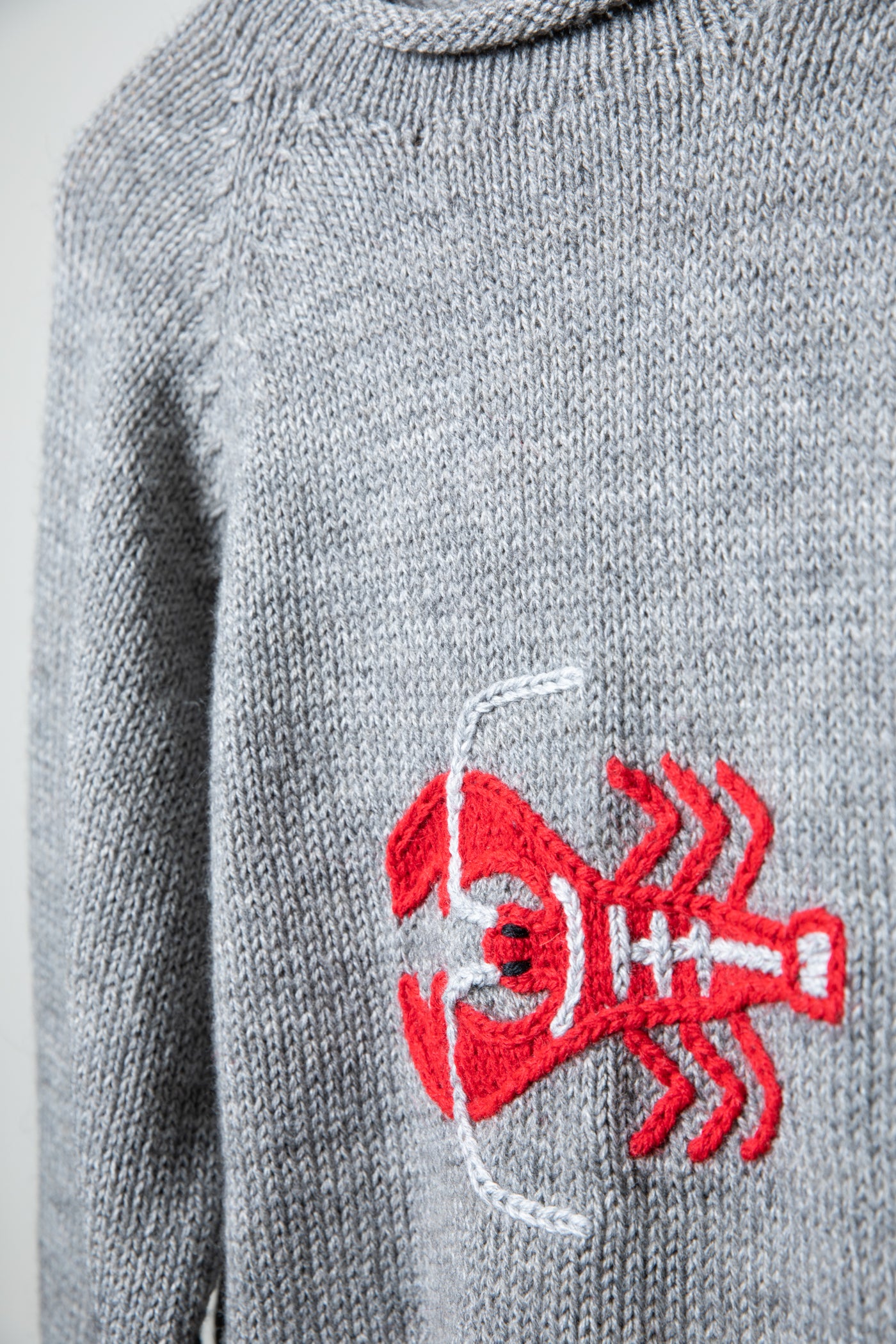 A close up detail of a knit lobster on a gray roll neck sweater made from alpaca wool. 