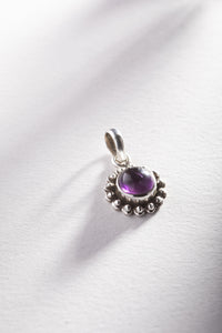 A round amethyst gemstone pendant set in a sterling silver floral design setting, photographed on a white background.